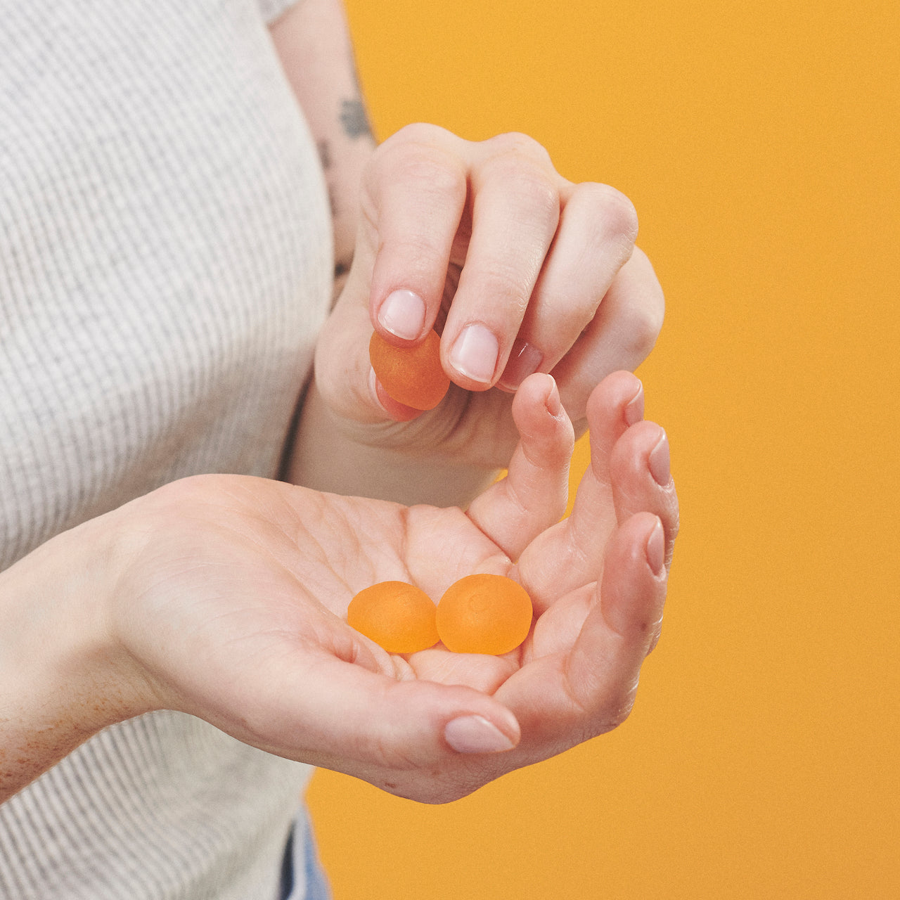 a closeup shot of 3 Feals Relax Gummies in a woman's palm against a yellow background